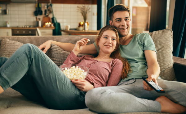 Young happy couple relaxing while watching TV and eating popcorn at home.