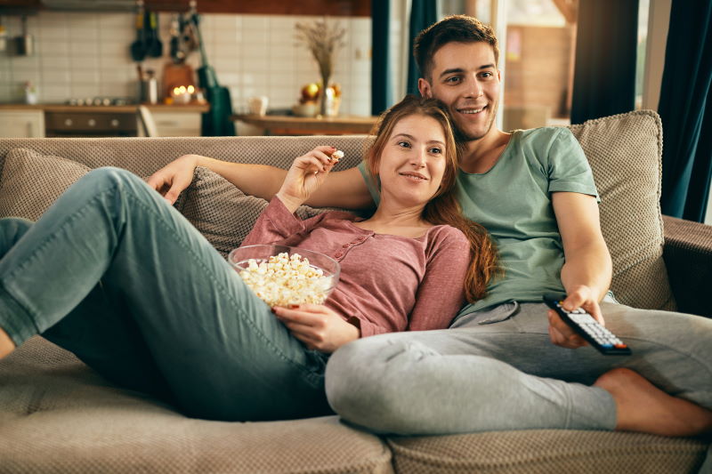 Young happy couple relaxing while watching TV and eating popcorn at home.